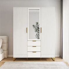 a white armoire with gold handles and drawers in a living room next to a bed