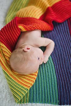 a baby wrapped in a rainbow blanket laying on it's side with its head resting on the top of his belly