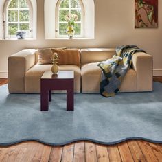 a living room with a blue rug and two windows on the wall, along with a beige couch