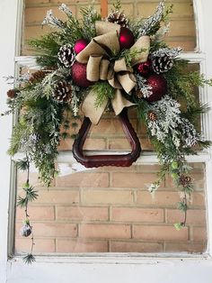 a christmas wreath hanging on the side of a brick building with pine cones and balls