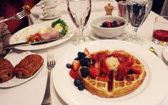 a waffle topped with fruit on top of a white plate next to croissants