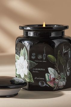 a candle that is sitting next to a jar with flowers on it and a lid