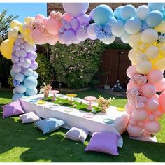 a table with balloons and flowers on it in the grass at a backyard party or event