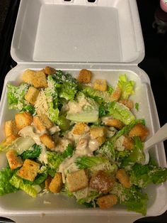 a salad in a foam container with dressing on the top and croutons sticking out of it