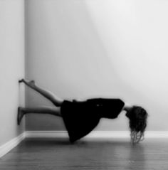 a woman standing on one leg in front of a wall with her legs spread out