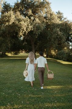 a man and woman walking in the grass holding hands, carrying baskets on their backs