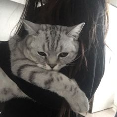 a woman holding a cat in her arms while wearing a black shirt with grey and white stripes