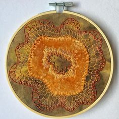 an embroidery project with orange and red designs on a white wall hanging from a metal hook