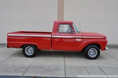 an old red pickup truck parked in front of a building