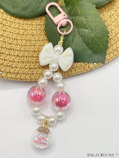 a pink and white beaded keychain hanging from a straw hat with green leaves