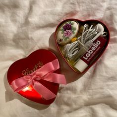 an open heart shaped box filled with personal care items next to a pink ribbon bow