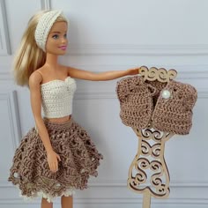 a doll is holding up a crocheted dress