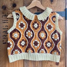 a brown and white crocheted sweater hanging on a wooden wall next to a hanger