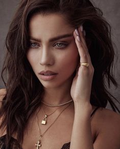 a beautiful woman wearing a gold necklace and holding her hand up to her face