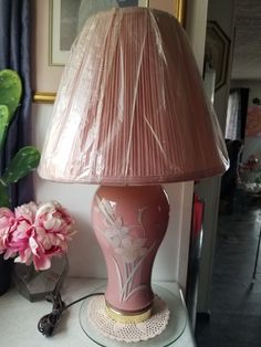 a pink lamp sitting on top of a table next to a vase with flowers in it