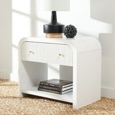 a white nightstand with books and a lamp on top