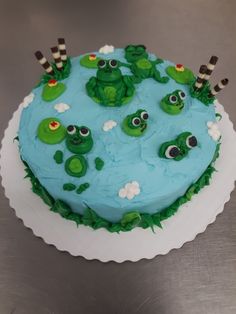 there is a cake decorated with green frogs on the top and blue frosting in the middle