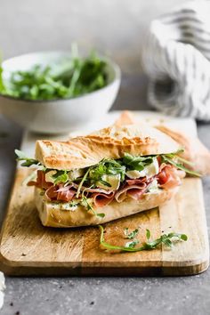 a sandwich cut in half sitting on top of a cutting board next to a bowl of salad