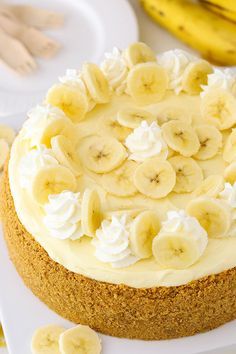 a cake with bananas and whipped cream on top sitting on a white plate next to sliced bananas