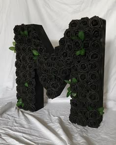 the letter k is made out of black paper roses and leaves, with green leaves on it