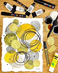 some markers and pens are sitting on a table next to an art work with yellow circles