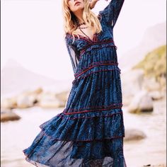 a woman in a blue dress is standing on the beach with her arms behind her head