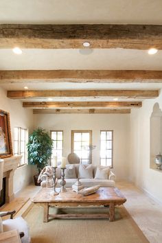 a living room with couches, tables and fireplace in the center is decorated with wood beams