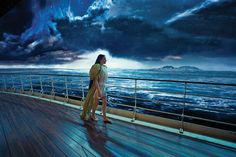 a woman standing on top of a wooden deck next to the ocean under a cloudy sky