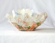 a glass bowl that is sitting on a white cloth covered tablecloth with flowers and leaves in it