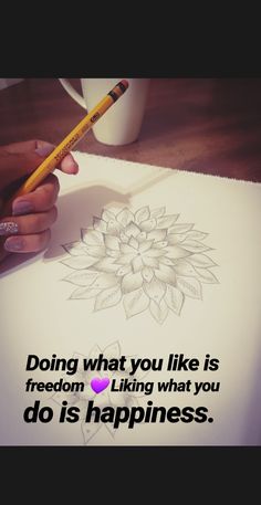 a person is drawing on paper with a pencil and cup in front of them that says doing what you like is freedom liking what you do is happiness