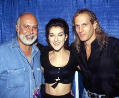 three people standing next to each other in front of a blue curtain and posing for the camera