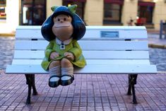 a stuffed animal doll sitting on top of a white bench in front of a building