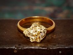 Material: 22k band                  22k gold nugget Size: 6.5 The band is a half-round, 3mm wide smooth 22k gold. The single chunky gold nugget is a beautiful natural nugget found by a prospector in Alaska. This nice little nugget is 10mm x 12mm in diameter. This is a nice chunky nugget that sits high on the ring. Gold in its natural form from this region generally assays around 22k in purity.  The ring weighs 5.04 grams and is size 6.5.  Note on size I can size this one UP by as much as 1 full Gold Nugget Ring, Natural Gold Nugget, Gold Miners, Gold Mining, Gold Nugget, Natural Gold, Natural Forms, 22k Gold, Real Gold