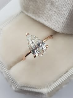 an engagement ring with a pear shaped diamond on it's side in a box