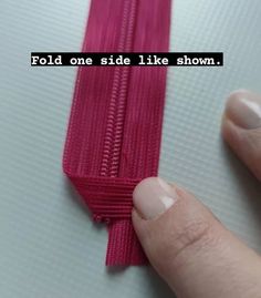 someone is holding the end of a pink zipper that has been pulled up with their thumb