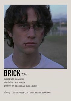 a young man with glasses stares at the camera in front of an advertisement for brick