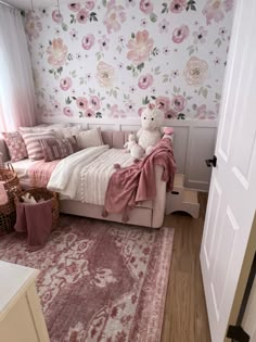 a pink and white bedroom with floral wallpaper on the walls, a teddy bear sitting on a bed