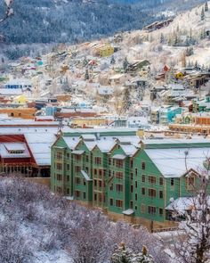 a green building with snow on the ground and trees in front of it, surrounded by mountains