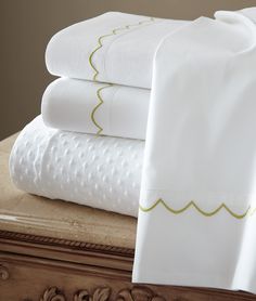 white sheets with gold scalloped trim on top of a wooden chest and drawer