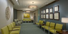 an empty waiting room with yellow chairs and pictures on the wall