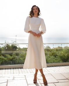 a woman wearing a white dress standing on a balcony with her hands in her pockets