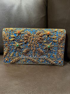 an ornate blue and gold purse sitting on top of a leather couch next to a pillow