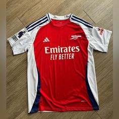 the shirt is red and white with blue trims on it, which says emirates's fly better