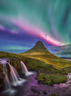 the aurora bore is visible above a waterfall and green grass covered hills with water running down it