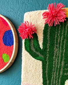 a wall hanging with a cactus and flower on it next to a round rug that has been embroidered onto the wall