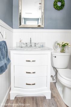 a white bathroom with blue walls and wood flooring is pictured in this image, there is a mirror on the wall above the sink