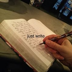 someone is writing on an open notebook with the words just write