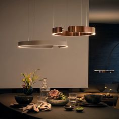 a dining room table with plates and bowls on it, lights hanging from the ceiling