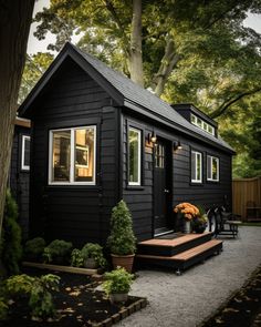 a small black house with white trim and windows on the front door is surrounded by trees