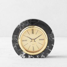 a black and gold clock sitting on top of a white table next to a wall